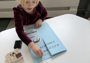 dzieci przy stołach wykonują karty pracy