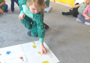 Dziewczynka układające plansze dydaktyczne na dywanie z dinozaurami