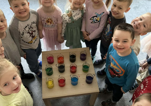 Dzieci na zdjęciu grupowym. Pomiędzy nimi stolik na którym, ustawione są szklanki z wodą zabarwioną bibułą