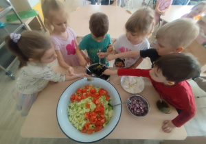 Dzieci wykonujące przy stole sałatkę grecką