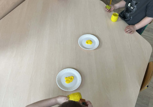 Dzieci malujące słoiczki żółtą farbą przy stolikach