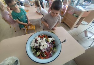 Chłopiec polewający sosem sałatkę grecką