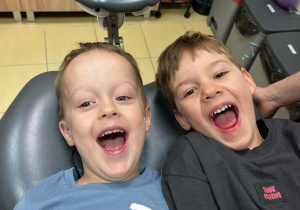 Chłopcy siedzący na fotelu dentystycznym uśmiechający się do zdjęcia