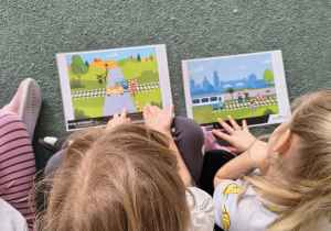 Dziewczynki oglądają ilustracje przedstawiające niebezpieczne sytuacje w pobliżu przejazdów kolejowych