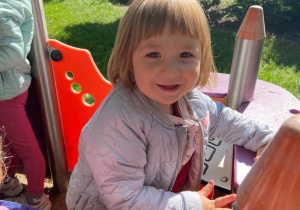 Dziewczynka uśmiecha się do zdjęcia w domku w ogrodzie przedszkolnym