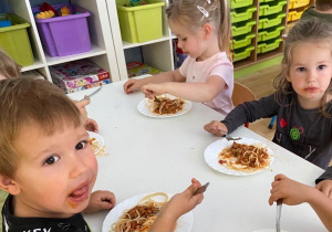Dzieci siedzą przy stoliku i jedzą obiad - spaghetti