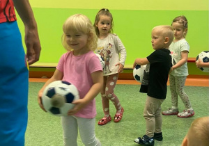 Dzieci na sali gimnastycznej wykonujący ćwiczenia z piłką nożną