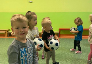 Dzieci na sali gimnastycznej wykonujący ćwiczenia z piłką nożną