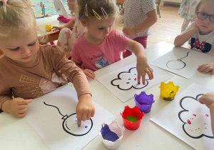 Dzieci wykonują prace plastyczną. Kropkują balony i chmury farbami za pomocą palców.