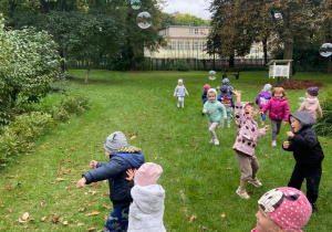 Dzieci gonią bańki w ogrodzie przedszkolnym.