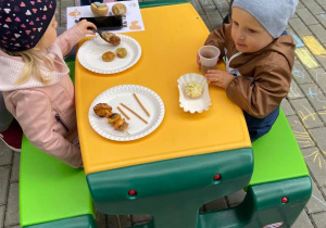 Dzieci siedzą przy stoliku na tarasie, jedzą potrawy z ziemniaka