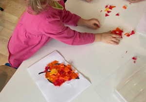 Dziewczynka przy stoliku wykonująca pracę plastyczną - liść wyklejany z bibuły
