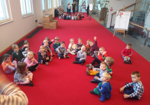 dzieci w oczekiwaniu na spektakl siedzą na czerwonym dywanie