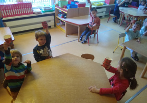 dzieci siedzą przy stole, piją sok jabłkowy w papierowym kubeczku