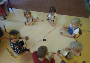 dzieci siedzą przy stoliku, malują farbami połówki ziemniaków