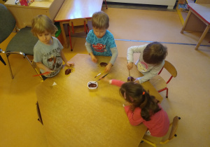 dzieci siedzą przy stoliku, malują farbami połówki ziemniaków