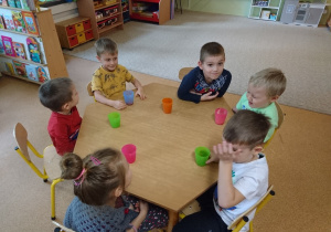 Sala przedszkolna. Dzieci siedzą przy stole, piją soki z kolorowych kubków.
