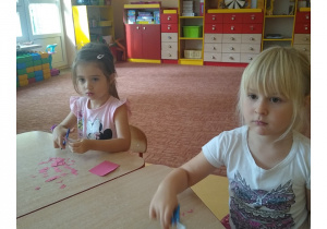 dzieci siedzą przy stoliku i wycinają różne kształty z papieru
