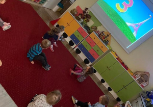 Dzieci w sali podczas zabaw rytmicznych przy ekranie ściennym