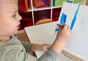 Chłopiec maluje flagę Francji farbami na płótnie umieszczonym na sztaludze