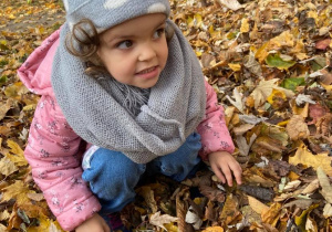 Dziewczynka w ogrodzie przedszkolnym pozuje w liściach