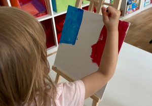 Dziewczynka maluje flagę Francji farbami na płótnie umieszczonym na sztaludze