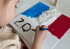 Dziewczynka maluje flagę Francji farbami na płótnie umieszczonym na sztaludze
