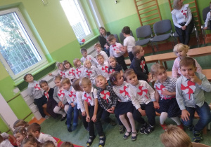 dzieci na sali gimnastycznej czekają na wprowadzenie flagi Polski