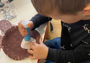 Chłopiec klei buzie misia do talerza pomalowanego na brązowo