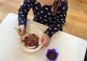 Dziewczynka maluje talerzyk papierowy na brązowo