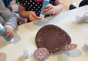 Dziewczynka klei buzie misia do talerza pomalowanego na brązowo