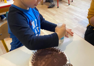 Chłopiec klei buzie misia do talerza pomalowanego na brązowo