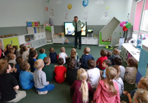 Sala przedszkolna. Dzieci siedzą na dywanie, oglądają prezentację funkcjonariusza Inspektoratu Transportu Drogowego.