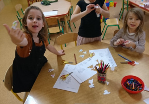 Dzieci siedzą przy stoliku, wycinają i kolorują postacie misiów. Gotowe pacynki z papieru zakładają na palce.