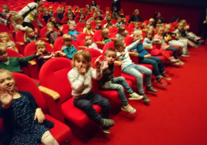 Widownia w teatrze Arlekin. Dzieci siedzą na krzesłach uśmiechają się, niektóre z nich machają