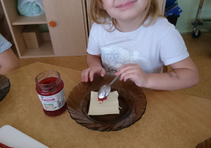 Sala przedszkolna. Dziewczynka siedzi przy stole i formuje ciastko z ciasta francuskiego.