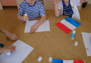 Sala przedszkolna. Dzieci siedzą przy stolikach wykonują flagę Francji.