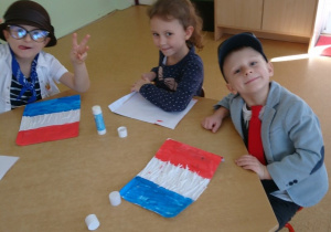 Sala przedszkolna. Dzieci siedzą przy stolikach wykonują flagę Francji.