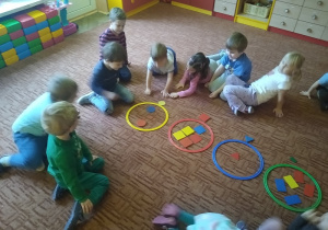 dzieci siedzą na dywanie, klasyfikują figury geometryczne