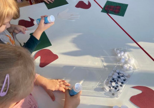 Dzieci przy stolikach tworzą kartki dla Świętego Mikołaja