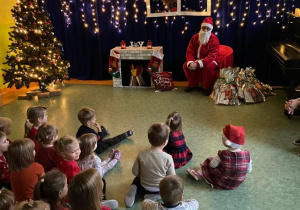 Dzieci na sali gimnastycznej siedzą i słuchają opowieści Świętego Mikołaja