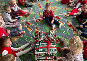 Dzieci w kole na dywanie oglądają prezenty od Świętego Mikołaja