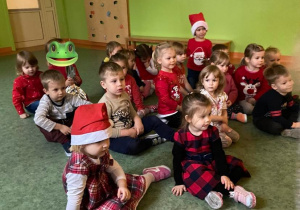 Dzieci siedzą na sali gimnastycznej podczas wizyty Świętego Mikołaja