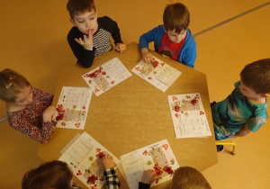 Sala przedszkolna. Ujęcie z góry. Sześcioro dzieci siedzi przy stoliku i układa wzór z różnych dodatków do czekolady.