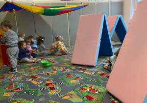 Dzieci w sali przedszkolnej z torem przeszkód z materacy oraz namiotem z chusty animacyjnej