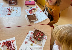 Dzieci przy stolikach. Przed nimi na podkładkach ułożone suszone owoce do ozdoby czekolady