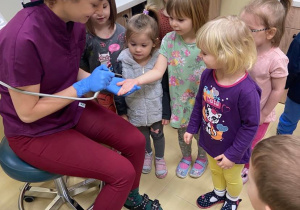Stomatolog pokazuje dzieciom jak wygląda przyrząd ze sprężonym powietrzem, dmucha dziewczynce w dłoń