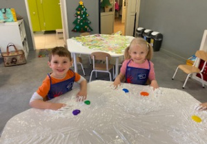 dziecko przy stoliku miesza dłońmi farby i łączy kolory