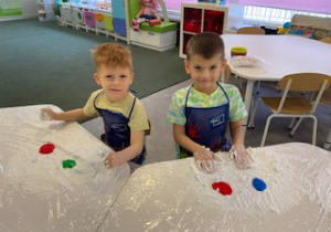 dziecko przy stoliku miesza dłońmi farby i łączy kolory