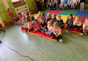 Dzieci siedzące w sali gimnastycznej na materacach